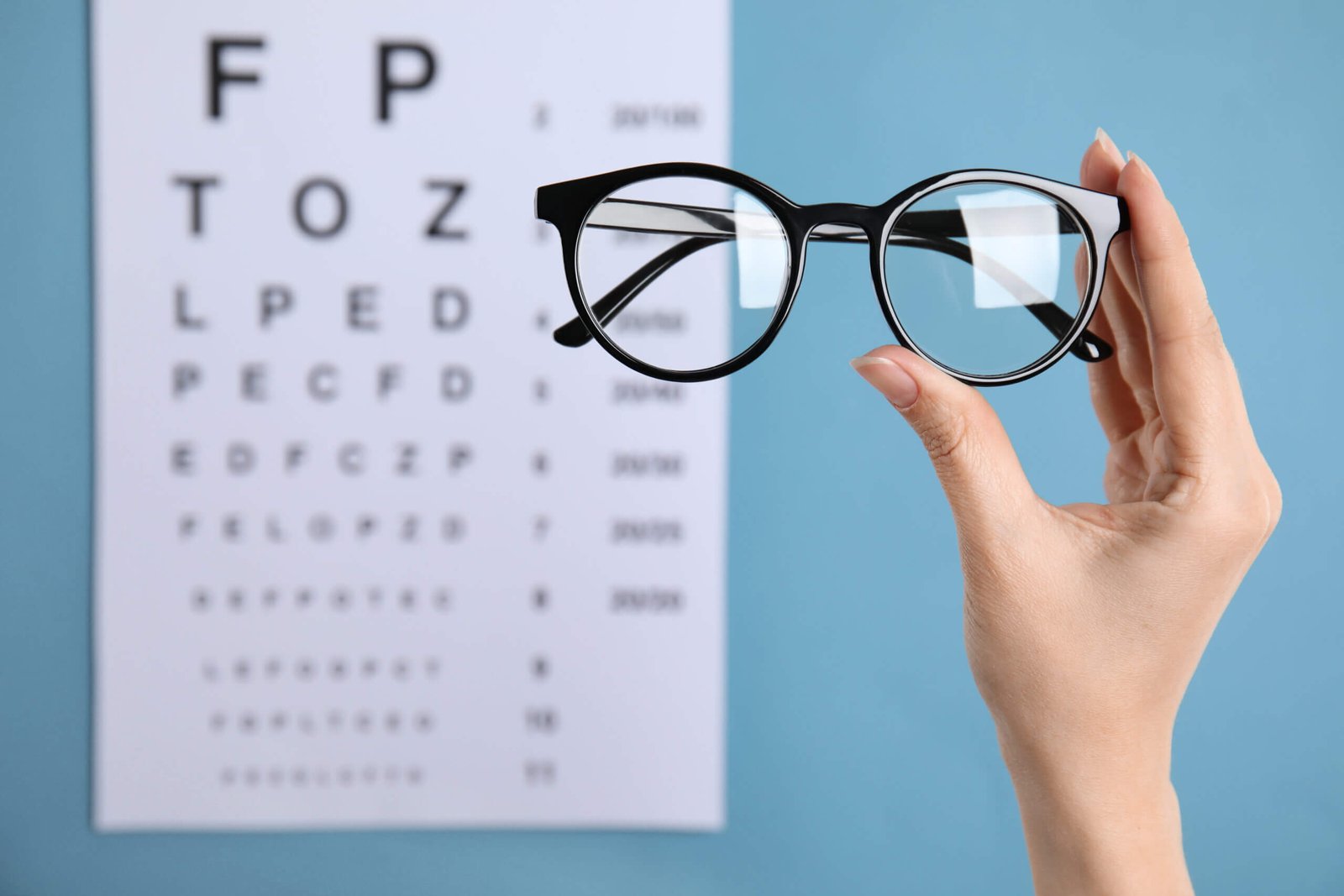 femme tenant des lunettes de vue devant un tableau de lettres pour un test visuel